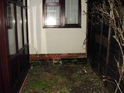 Base of brick wall with green growth from rainwater splash up.